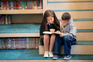 2 young students reading books together on the library stairs.
