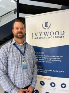 Picture of Ivywood Classical Academy Dean of Students Ben Ransier in front of an Ivywood branded standing-poster.
