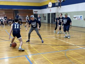 Photo from Ivywood Classical ACademy's inaugural staff vs. students homecoming basketball game, student dribbles basketball past staff member on basketball court.
